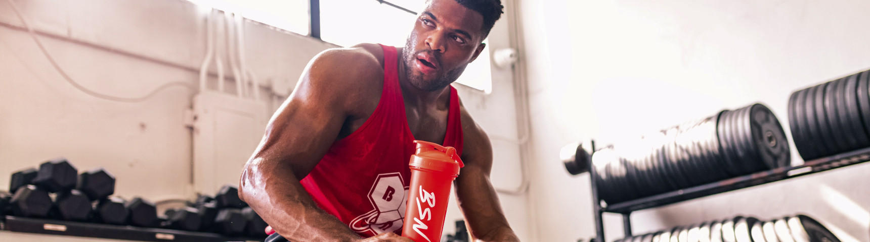 Man holding a BSN shaker bottle in a gym setting with weights in the background.