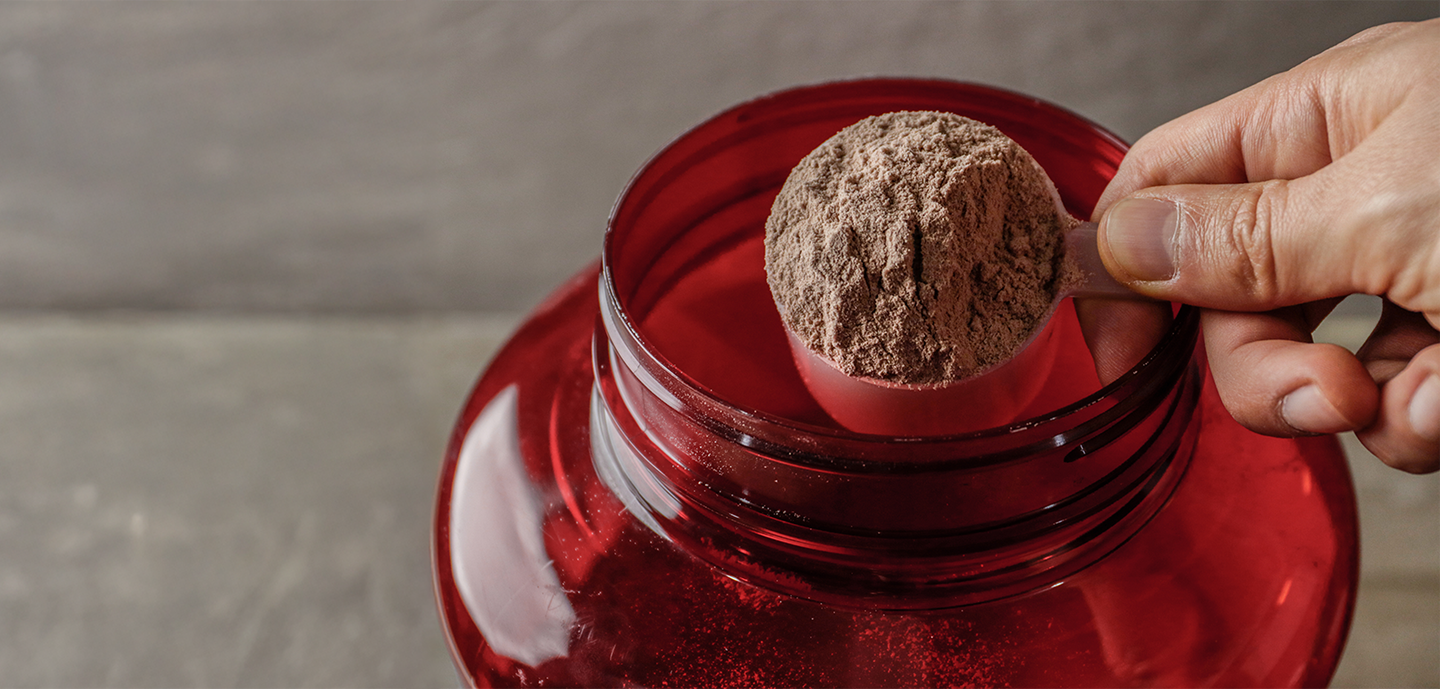 Scoop of protein powder being taken from a large red container.