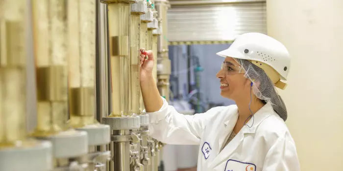 A person in a lab coat and helmet operates machinery in a laboratory setting.