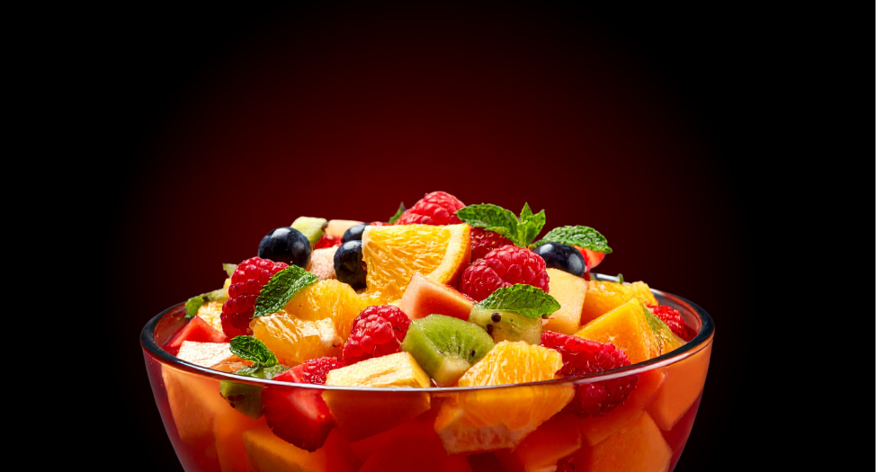 Fruit salad in a glass bowl with assorted fresh fruits like oranges, strawberries, and kiwi.
